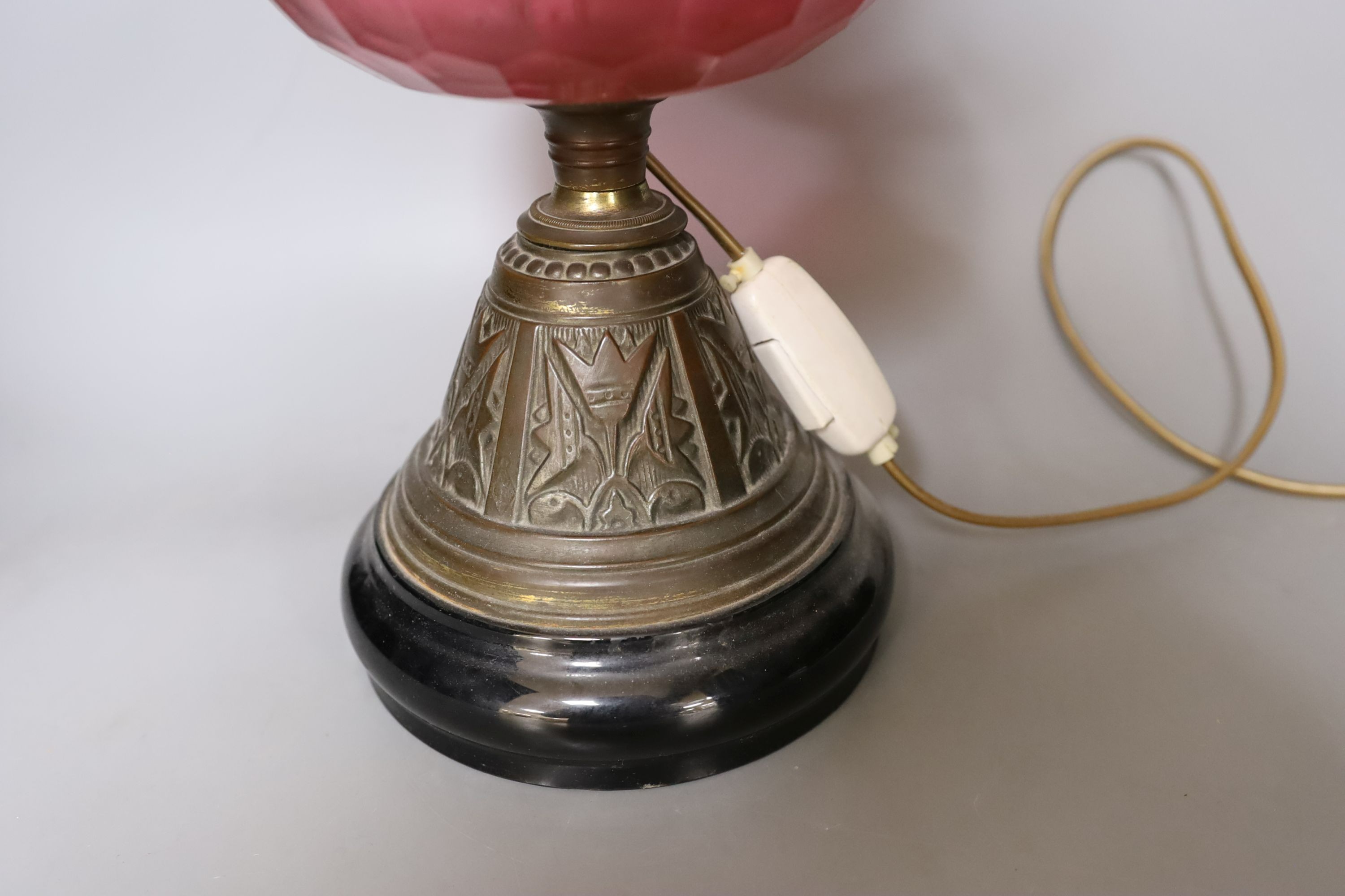 An Edwardian oil lamp with ruby glass font, later inverted to electricity, 57 cms high including funnel.